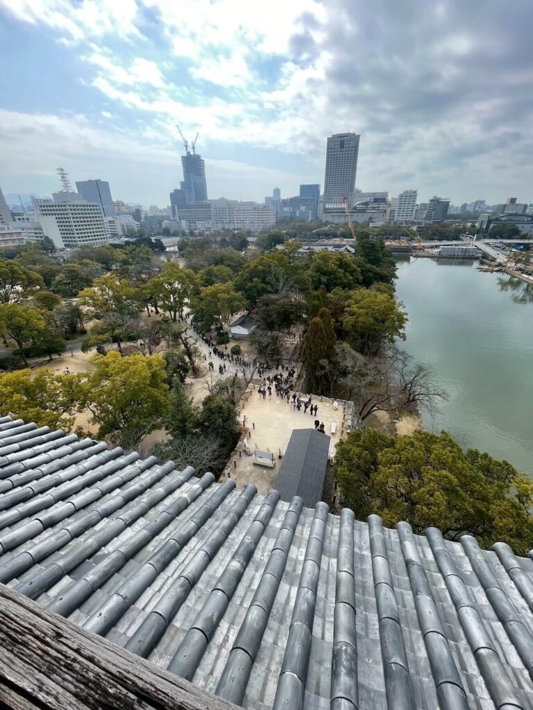 広島城天守閣の最上階から見下ろす広島の街並み。手前にはお城の瓦屋根、奥にはビル群が一望できる。