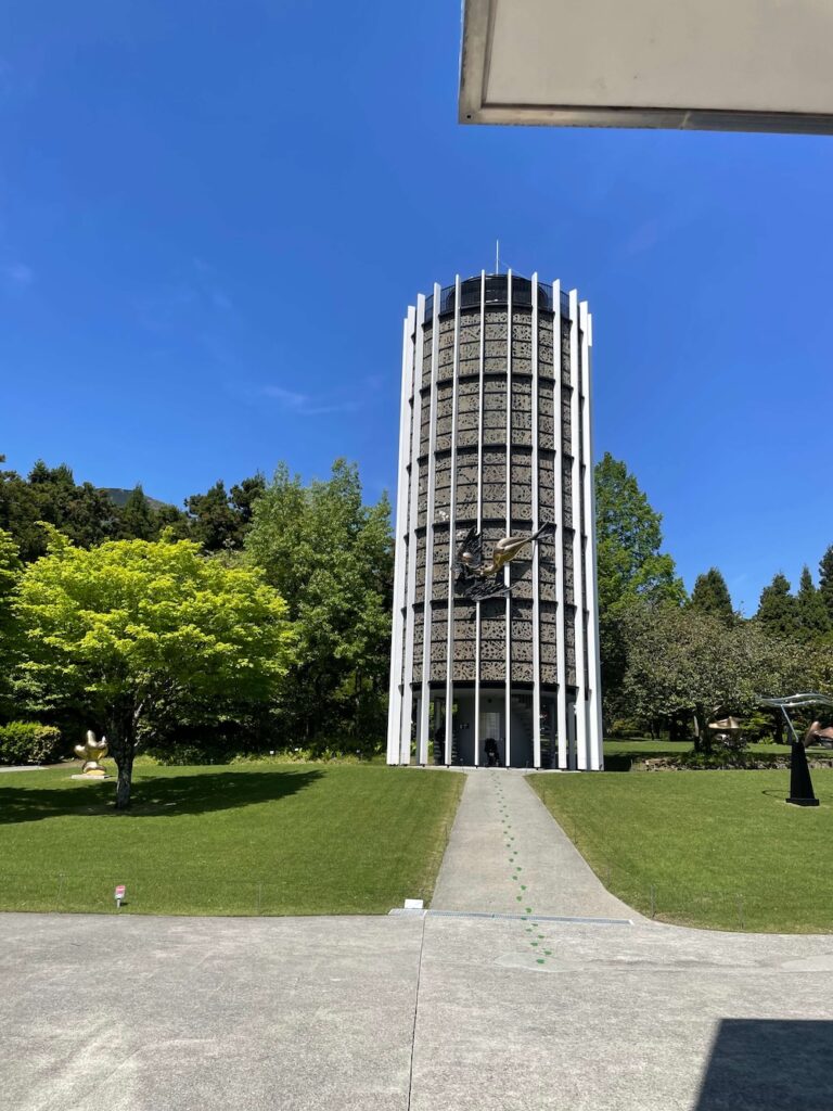 芝生の広場の奥に立つ、彫刻の森美術館の「幸せをよぶシンフォニー彫刻」の塔の外観 遠くからでも目を引く「幸せをよぶシンフォニー彫刻」の塔。